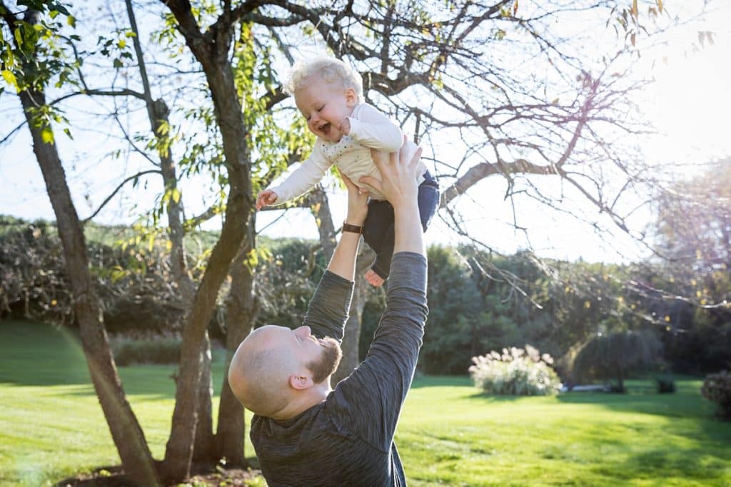 dad lifts baby girl into the air outside in backyard