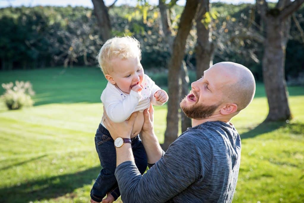 dad lifts baby girl into the air outside in backyard for a fun and stress free family photo session