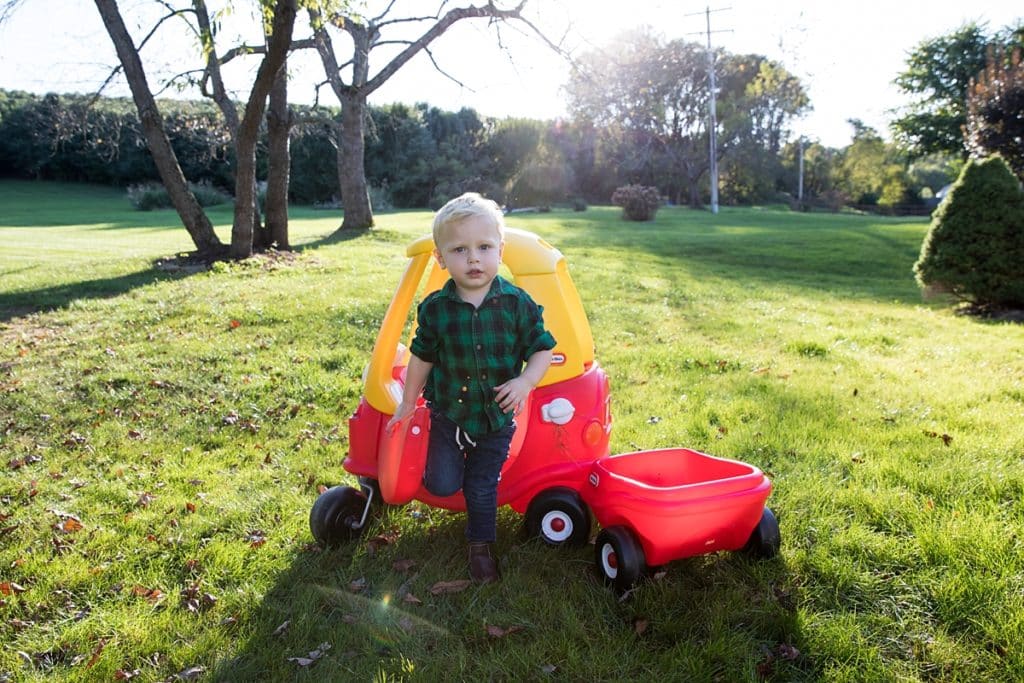 toddler stands next to cozy coupe car outside in backyard for a fun and stress free family photo session