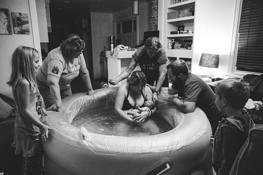mom delivers own baby in birthing pool in living room with husband, midwife and daughter for homebirth