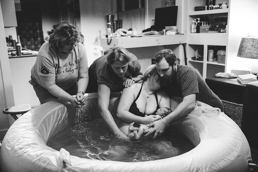 mom delivers own baby in birthing pool in living room with husband, midwife for homebirth