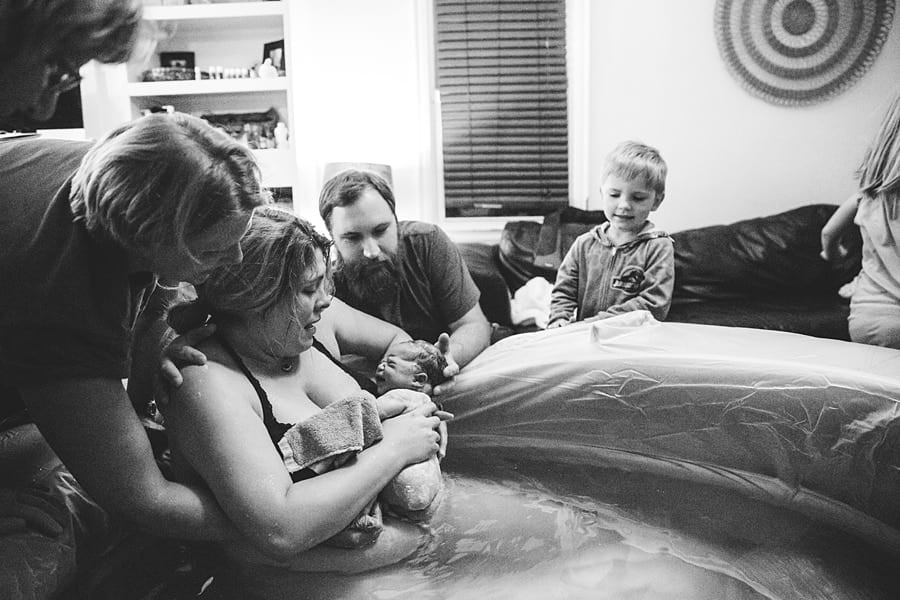 mom delivers own baby in birthing pool in living room with husband, midwife and daughter for homebirth