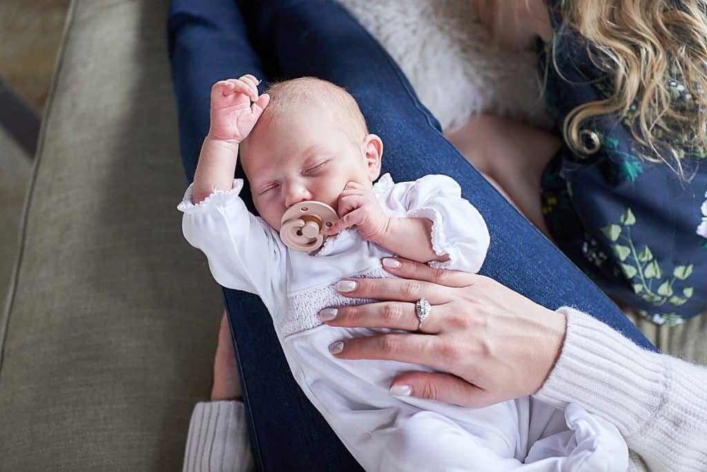 newborn baby with pacifier laying on moms lap with hand over her head