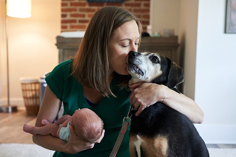 mom kissing dog and holding newborn son