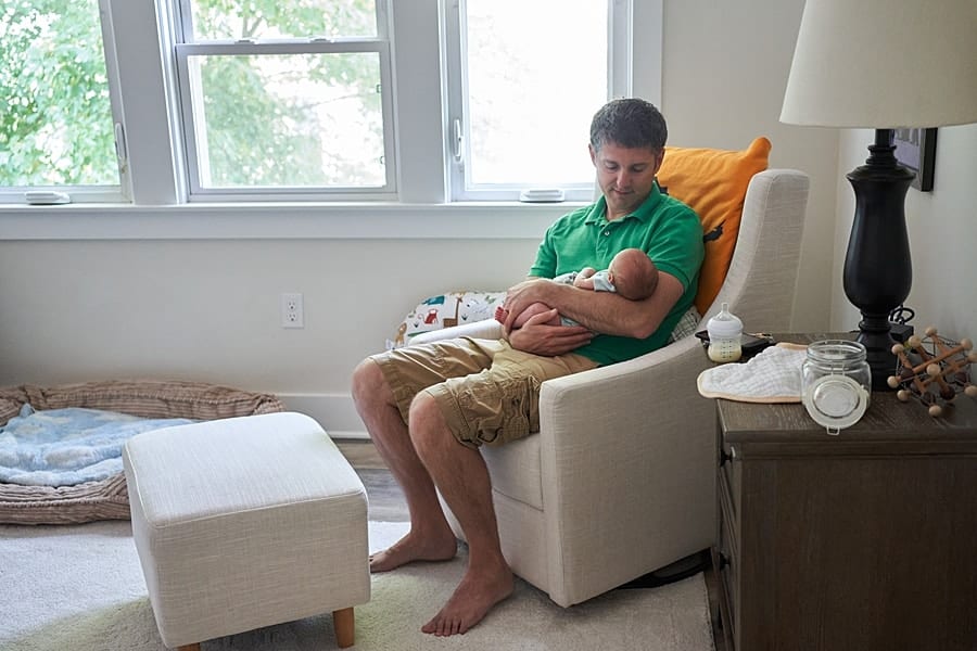 dad looking at newborn son in glider rocker in nursery