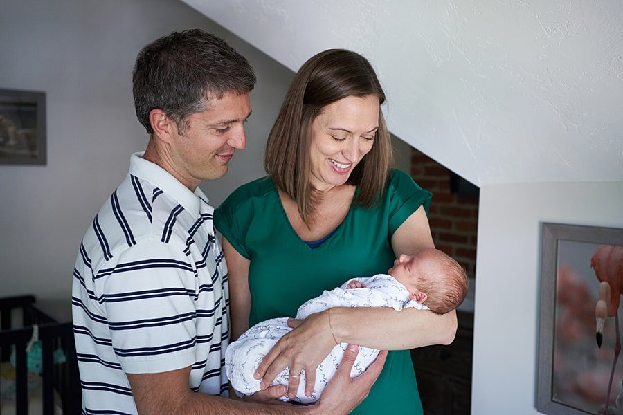 mom and dad looking at newborn son in nursery in their home