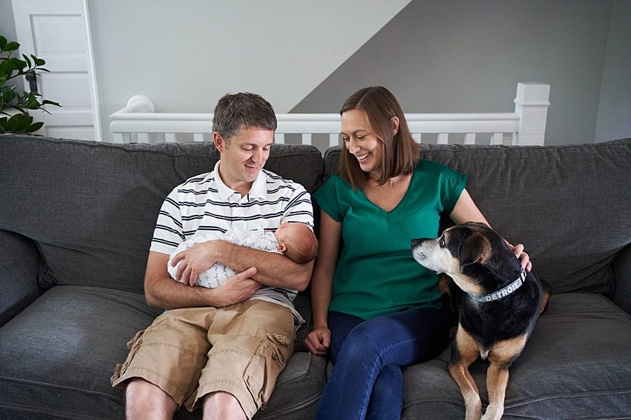 mom and dad looking at newborn son on living room couch with dog