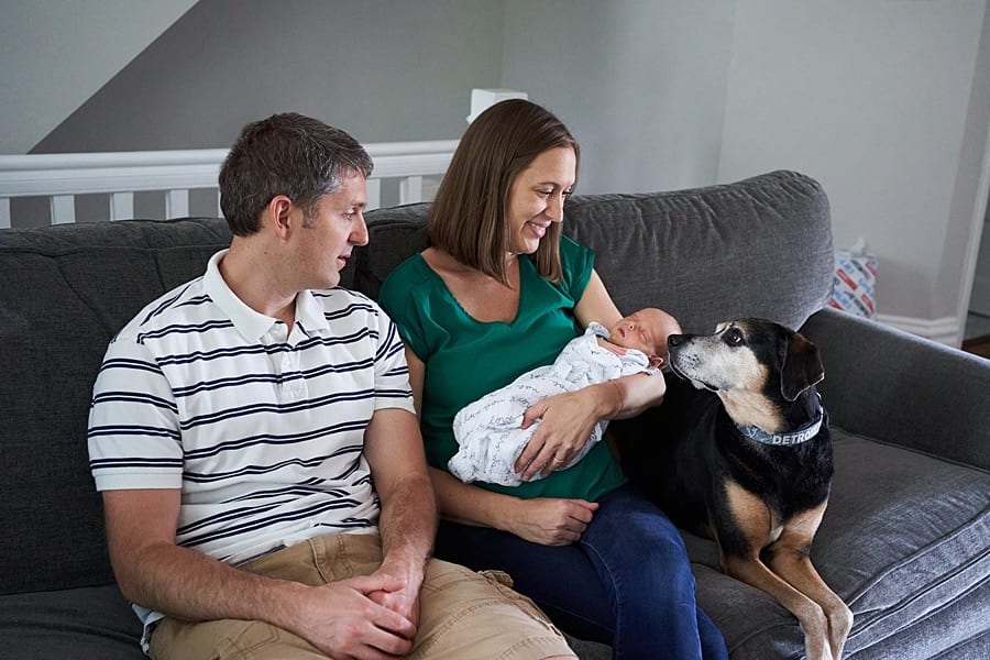 mom and dad looking at newborn son on living room couch with dog