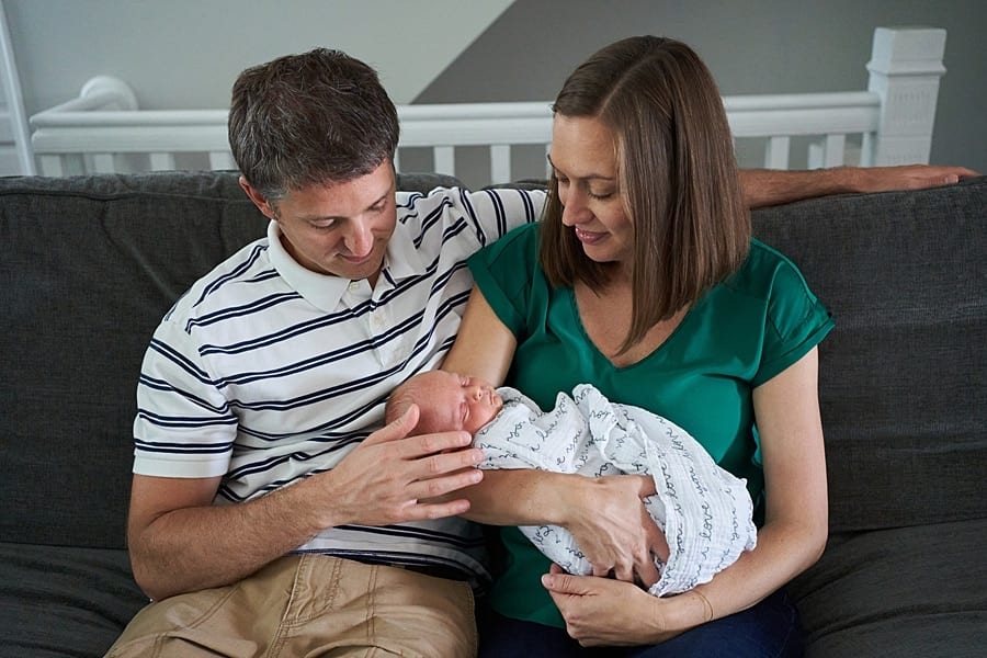 mom and dad looking at newborn son on living room couch