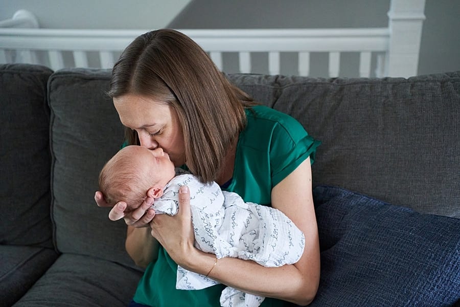 mom kissing newborn son on living room couch