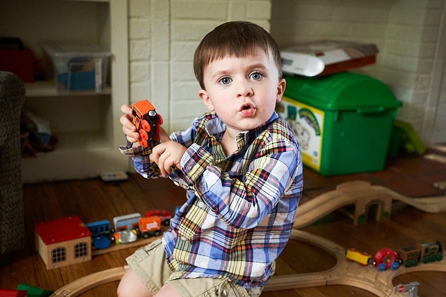 Toddler holding a Thomas the train engine pointing to it and looking into the camera