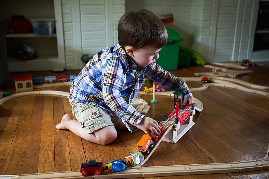 Toddler playing with Thomas the train engines and wooden trap in living room floor