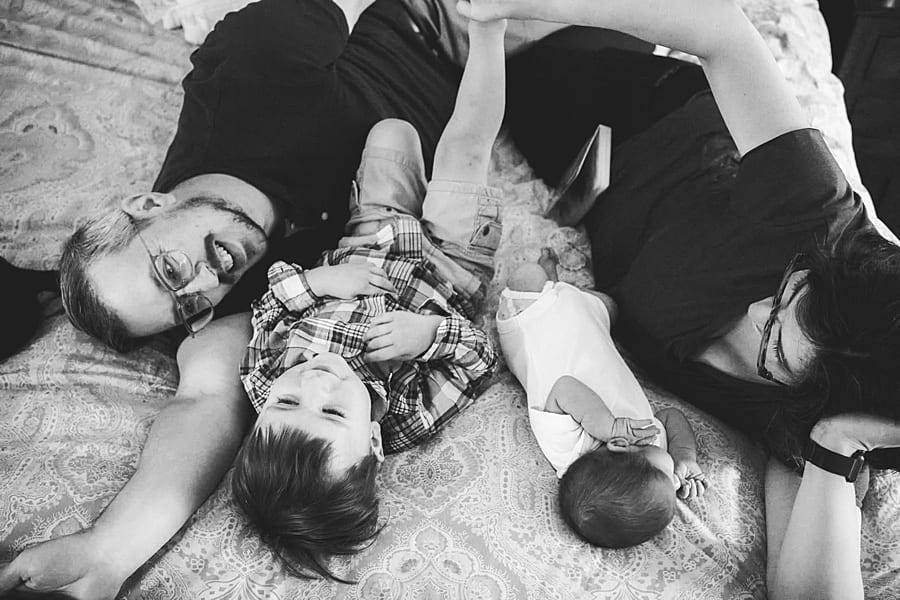 mom and dad with toddler and newborn laying on bed