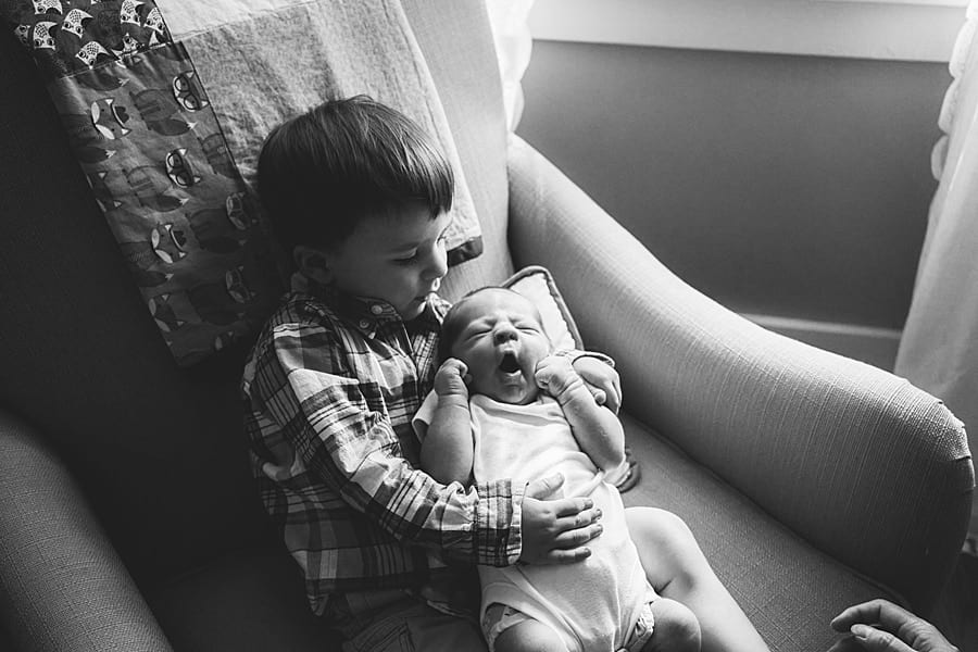 big brother sibling holding newborn brother in rocking chair for photo session 