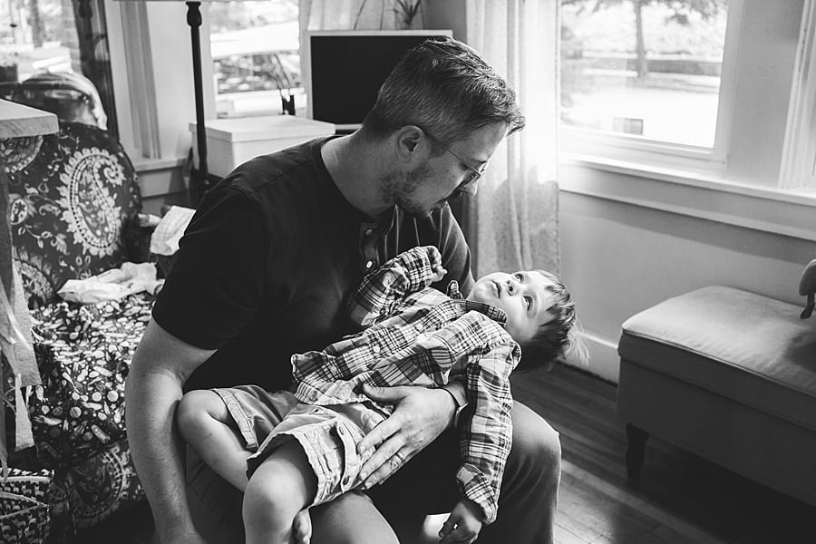 Father holding toddler son on his lap gazing out the window and black and white in sunroom