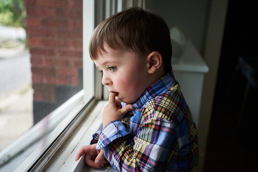 toddler with finger in mouth looking out the window