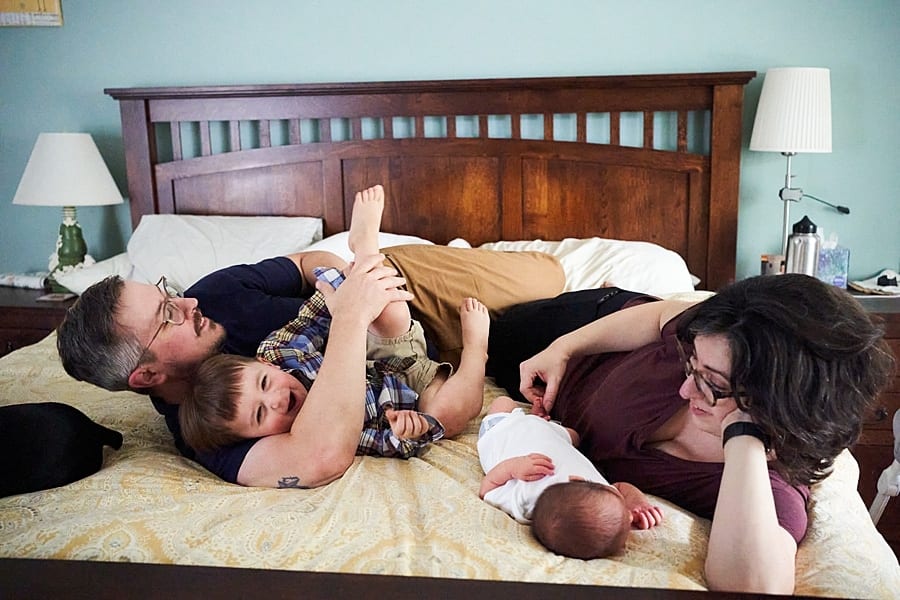 dad wrestling on bed with toddler while mom and baby lay next to them