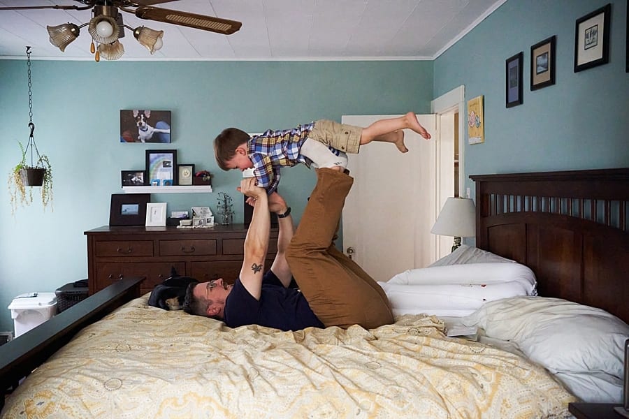 dad playing airplane with son up on his feet on bed