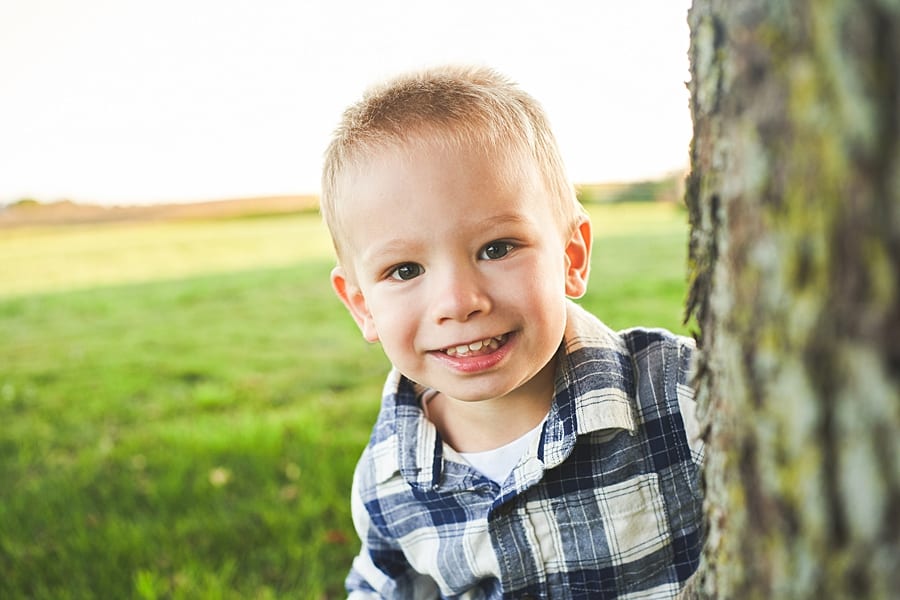 Little boy playing peekaboo behind a tree smiling and looking into the camera