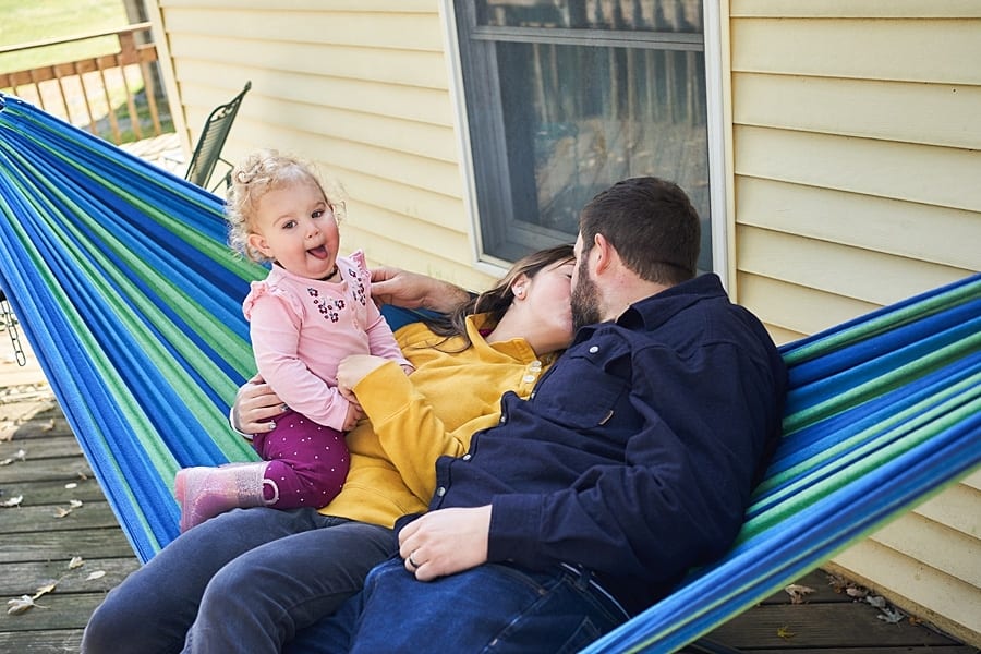 Mom and dad kissing on hammock while little girl sticks out her tongue