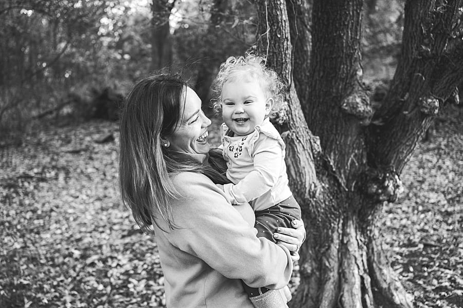 Mother holding smiling daughter with curly hair next to tree