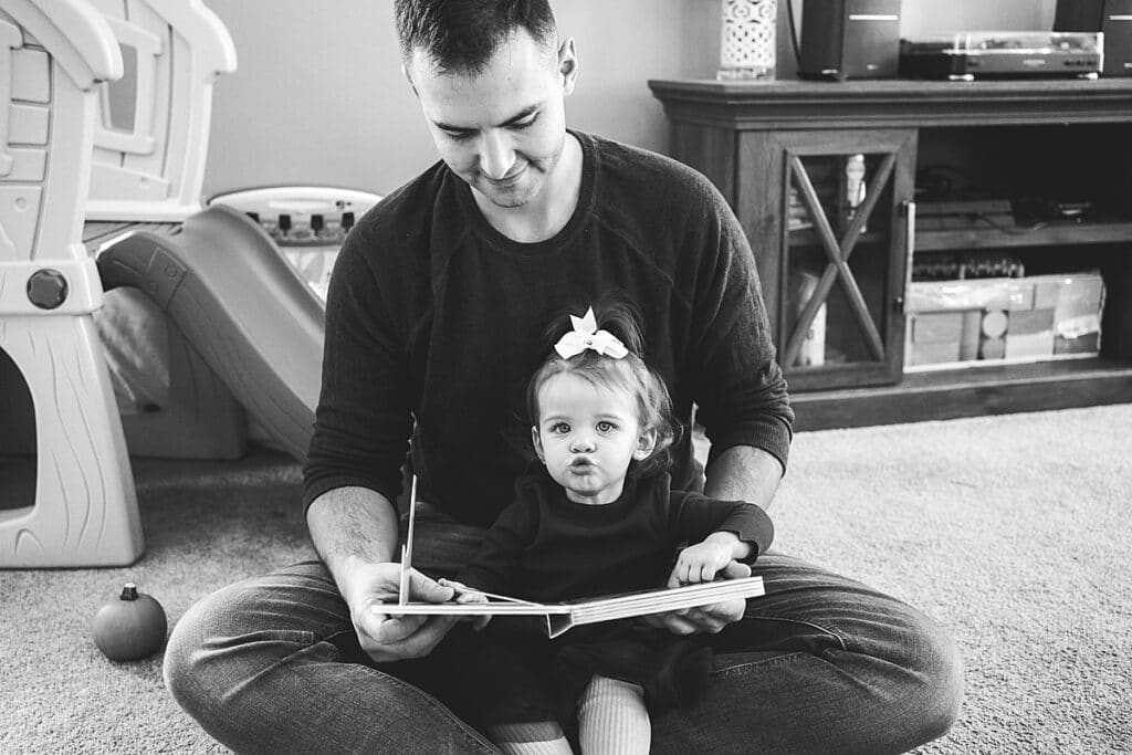 Father with toddler girl sticking her lips out reading a book