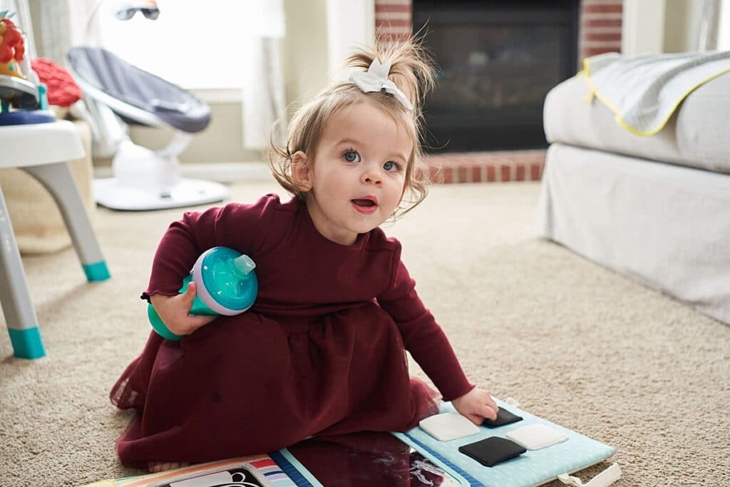 Little girl crouched on floor looking at a book holding a sippy cup