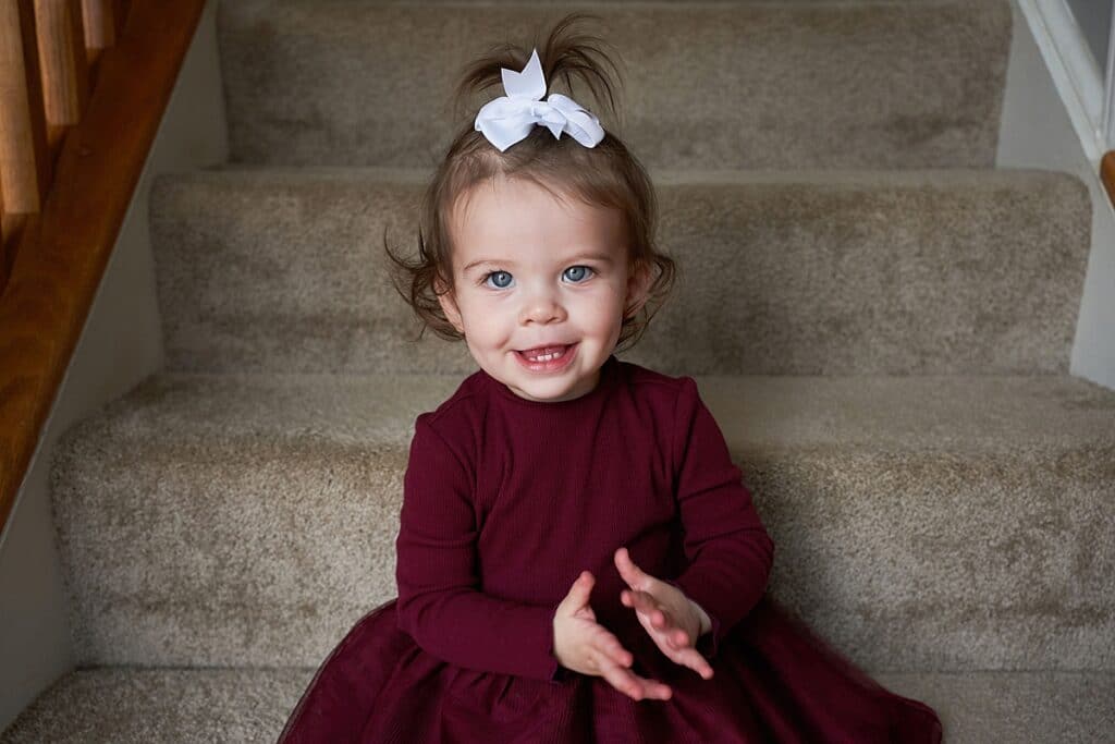 Little girl with a bow on top of her head sitting on the steps looking into the camera and smiling