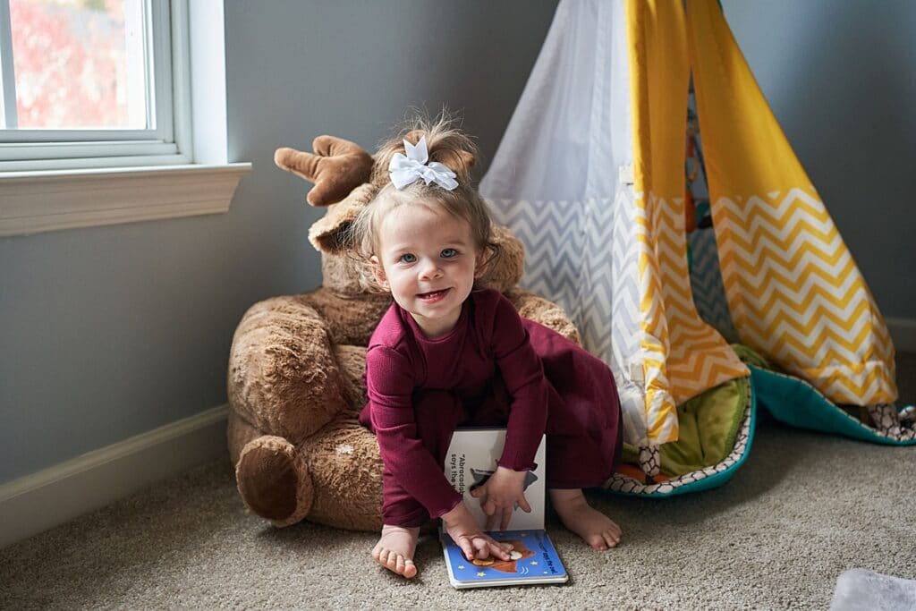 Little girl smiling and looking at the camera sitting on a stuffed moose chair in front of a Teepee