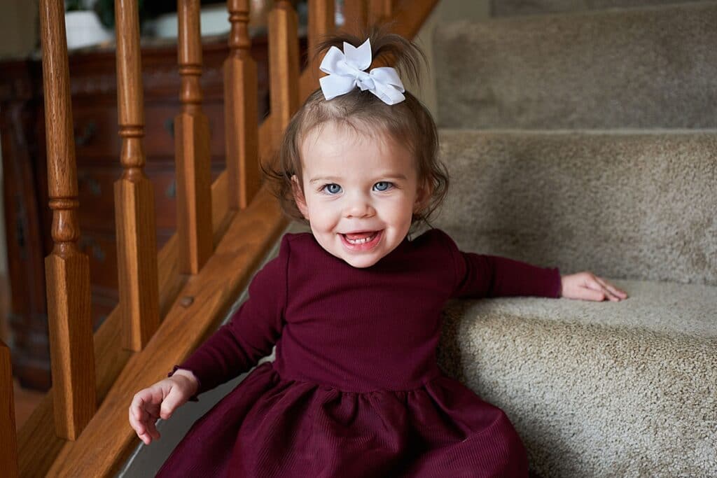 Little girl with a bow on her head sitting on steps smiling and looking into the camera