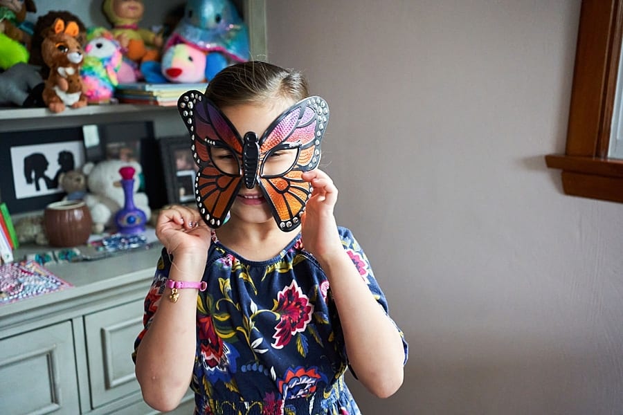 Little girl wearing a monarch butterfly mask standing in her bedroom