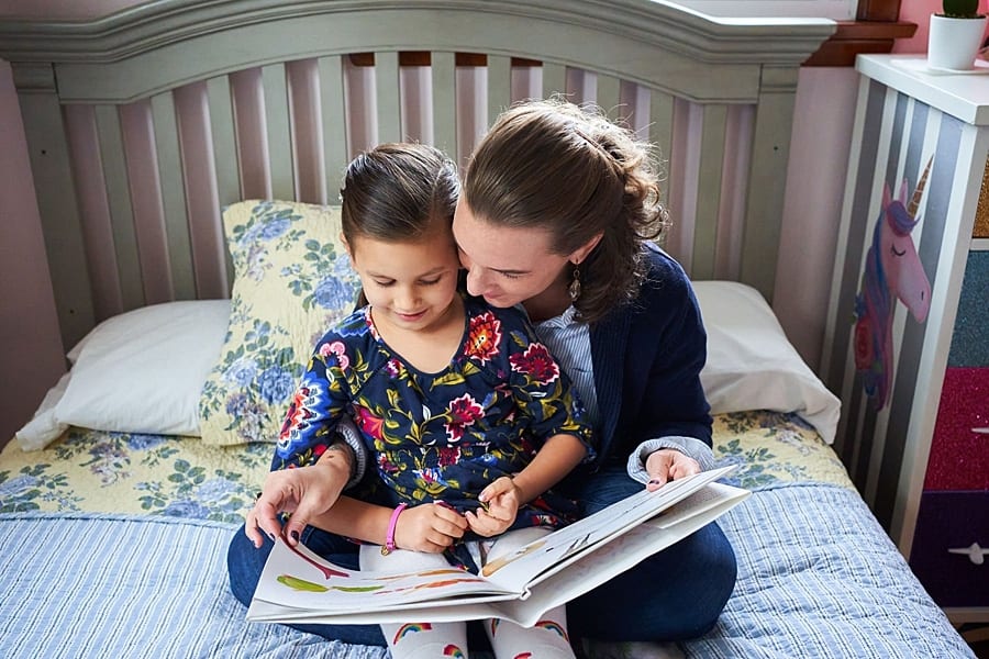 mother reading daughter a book in bed bat home