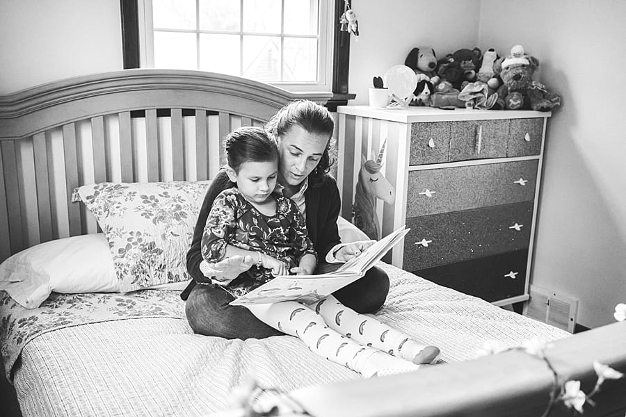 mom reading a book to daughter on bed in home