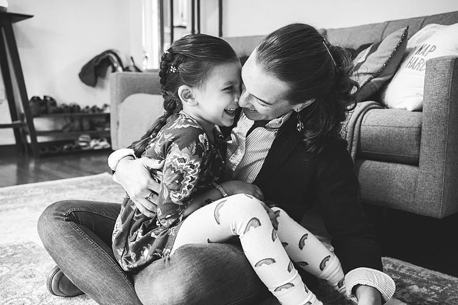 Mother and daughter cheek to cheek laughing and smiling sitting on living room floor