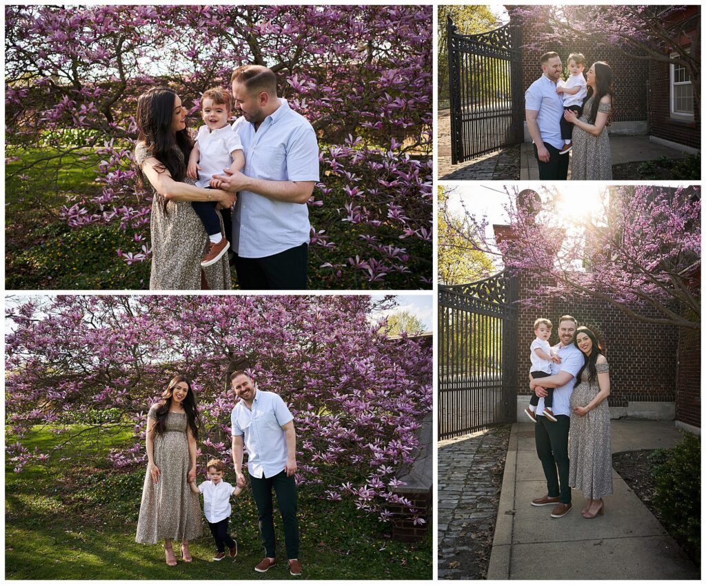 A family of three poses together outdoors near blooming trees and a brick gate on a sunny day, capturing the beauty of spring blossoms during photo sessions in Pittsburgh.