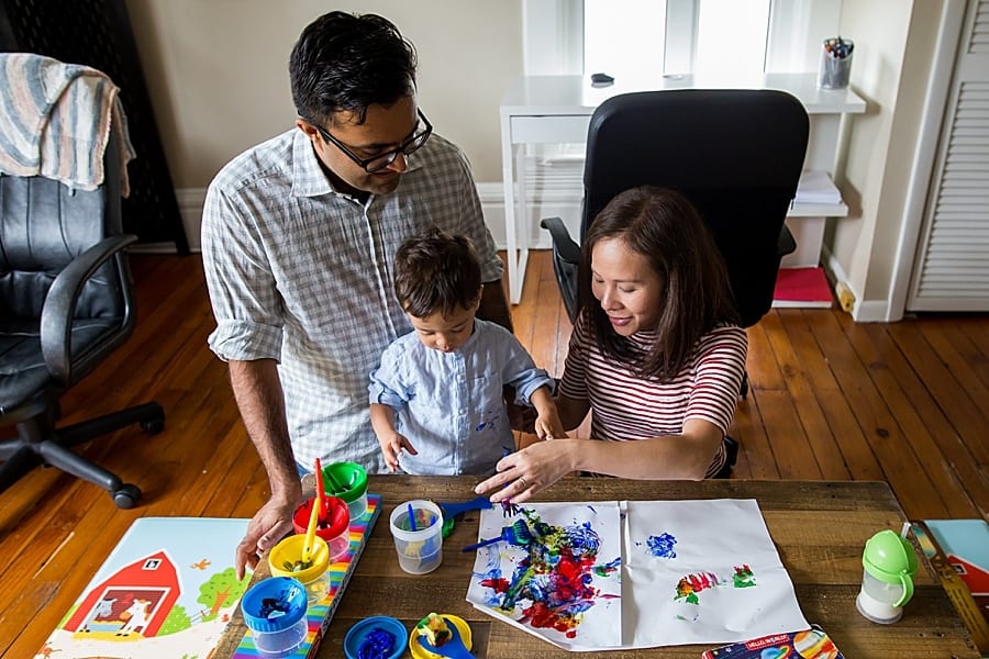 mom and dad sitting on floor at small table with toddler son and messy paints