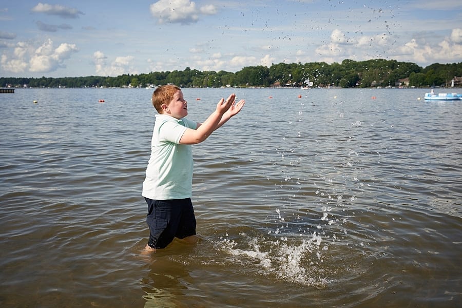 Little boy standing in lake splashing water in a polo shirt