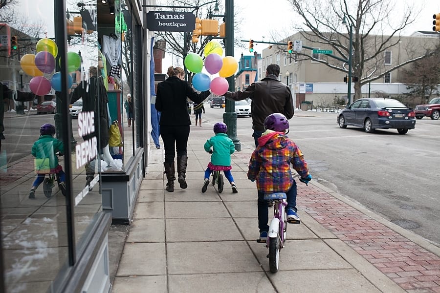 10 ideas for an on-location family photo session around Pittsburgh girls on bike on the sidewalk in downtown Beaver follow and parents caring balloons in front of bakery