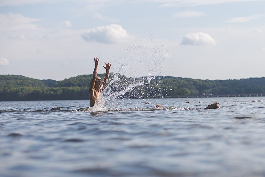 Boy in lake with arms above his head splashing brother with water