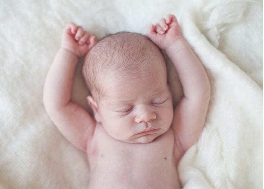 posed newborn photo session newborn baby sleeping with arms up overhead laying on cream fuzzy blanket