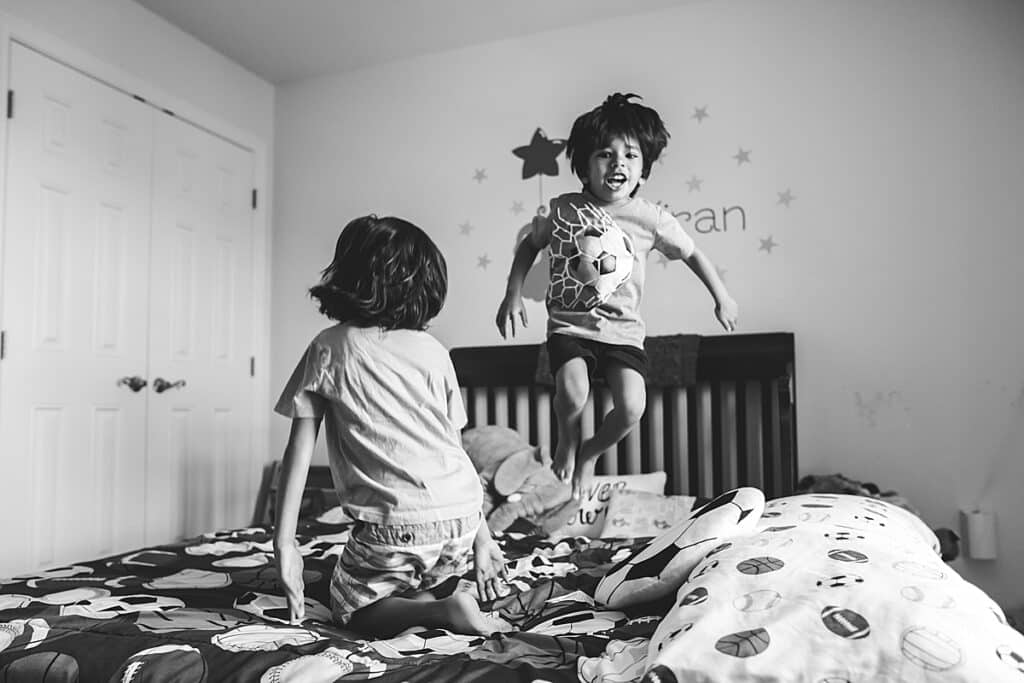 brothers with dark hair jumping on the bed in their bedroom