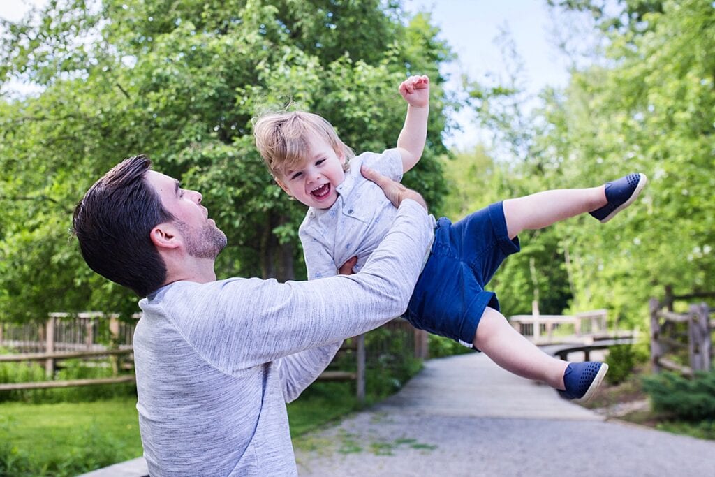 father swinging toddler son up in the air for an outdoor family photo session at the beechwood nature reserve in pittsburgh  