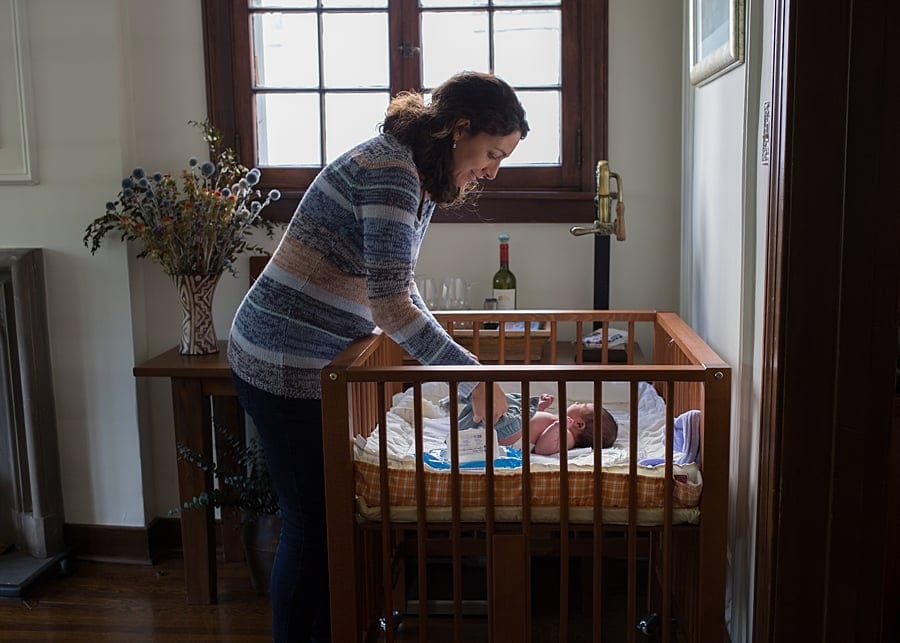 mom looking into crib in Canfield living room lifestyle newborn photo session 