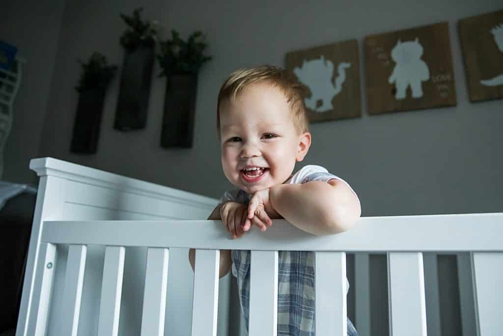 toddler boy in crib smiling and laughing looking into camera