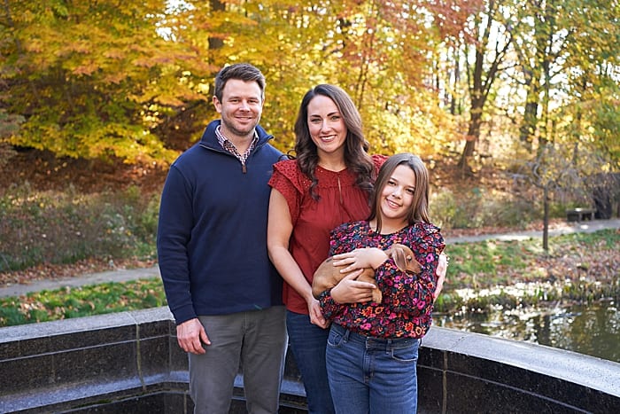 mother father and daughter with puppy by pond of Westinghouse Memorial in Schenley park for a family photo session