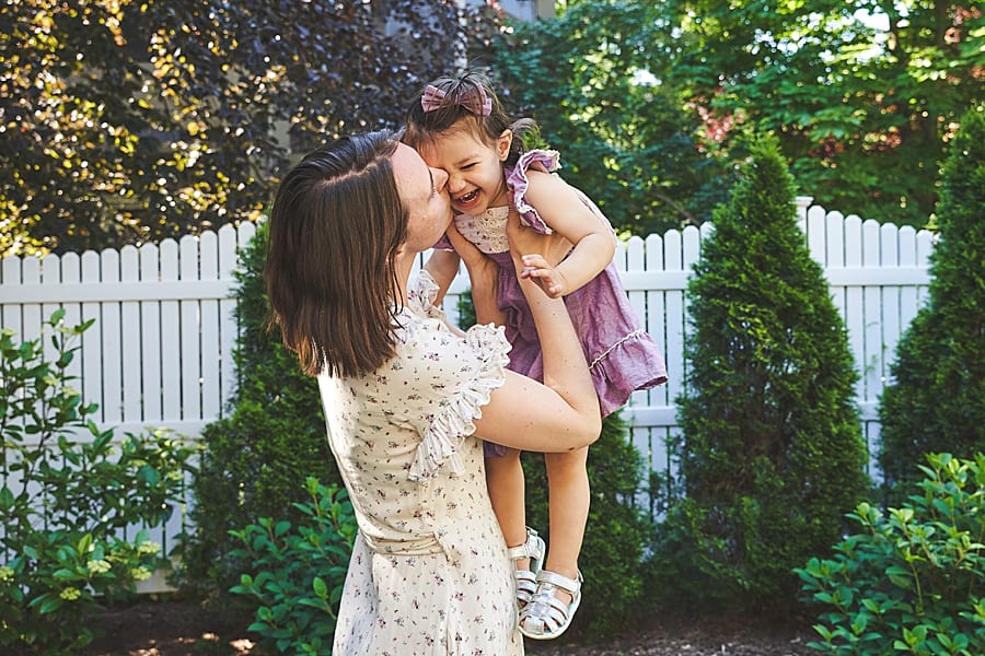 mom kissing daughter in backyard for photo session with Shadyside newborn photographer