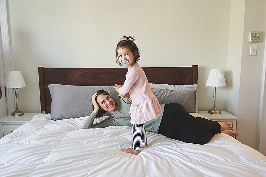 mom dad and little girl playing on the bed in master bedroom of Shadyside home for a family photo session 