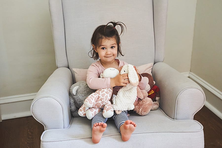toddler girl in chair in nursery of Shadyside home with stuffed animals