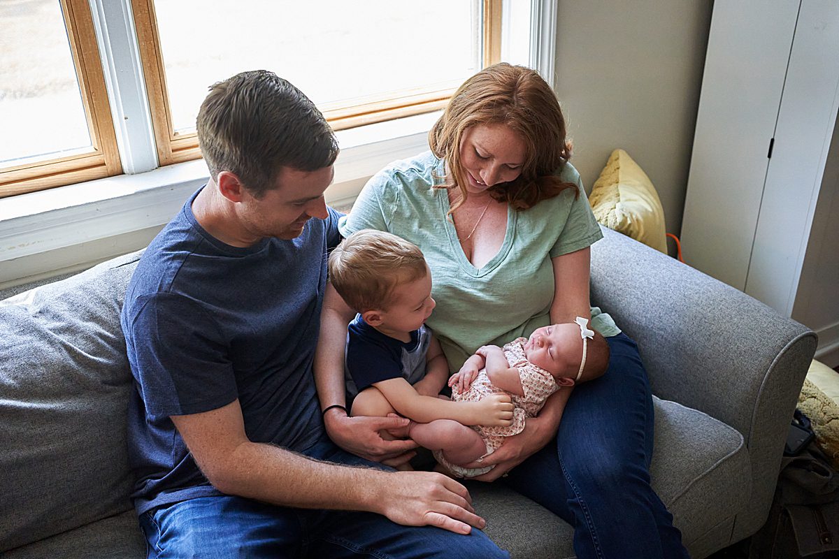 mom and dad with toddler and newborn on the couch for an in home newborn photo session