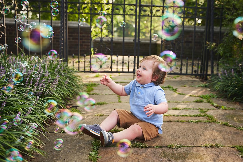 wexford baby with bubbles during a photo session at the walled garden in Mellon Park with black metal gates and brick walls and flowers